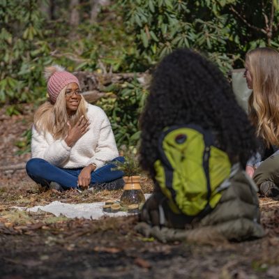 forest therapy tea ceremony with a women of color sitting in a circle smiling at forest therapy guide.