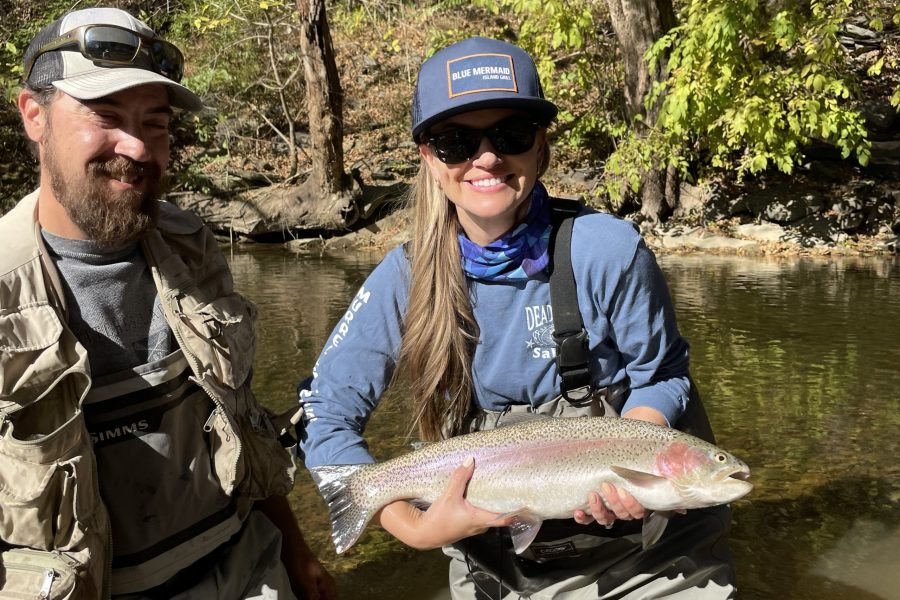 Male fishing guide with vest on stands next to women with large trout while floating Shenandoah River.