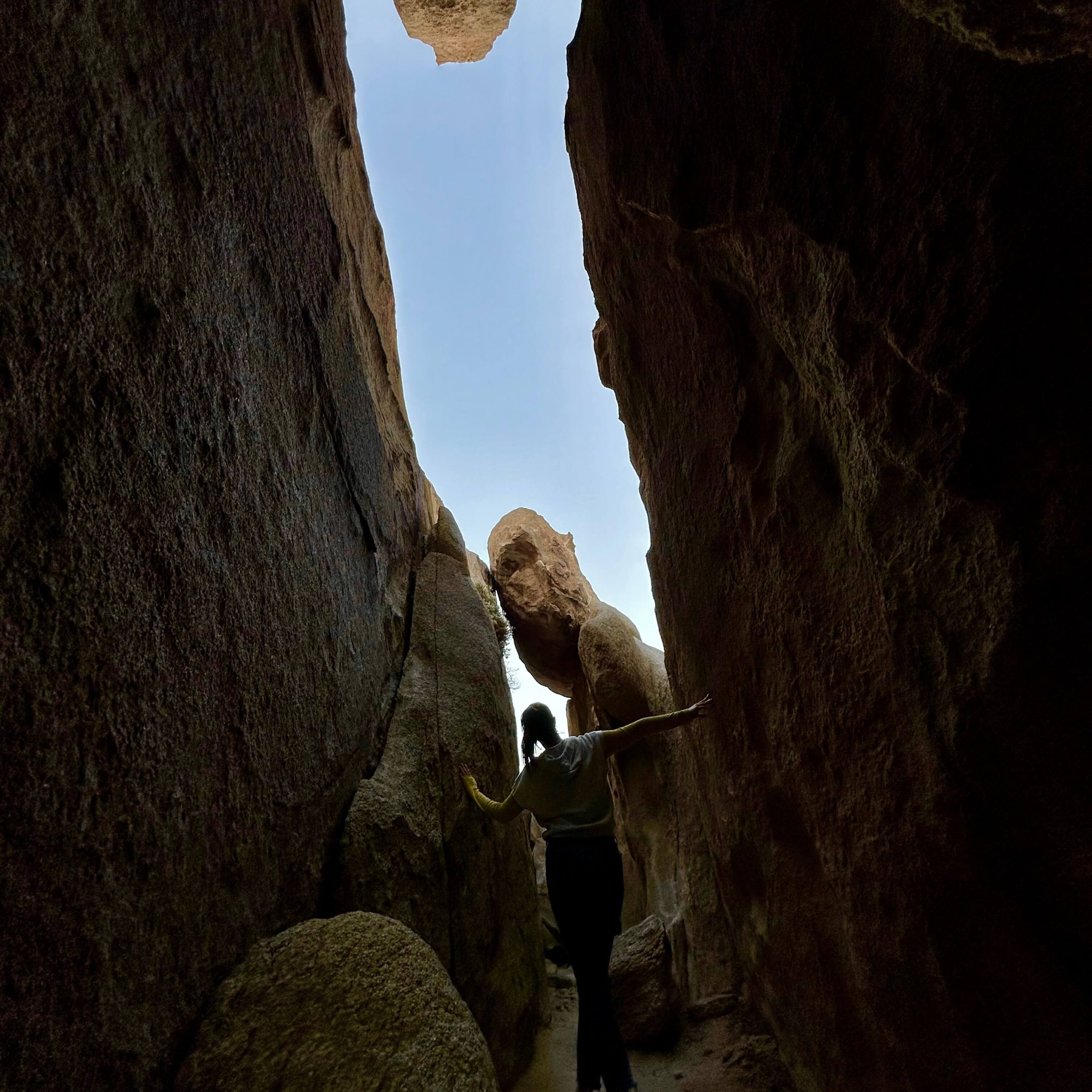 A women with arms outstretched walked away from the tours cave toward bright blue sky with rock formations before her.