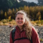 women with blonde hair in pony tail smiling at the camera with Alaskan yellow trees in background