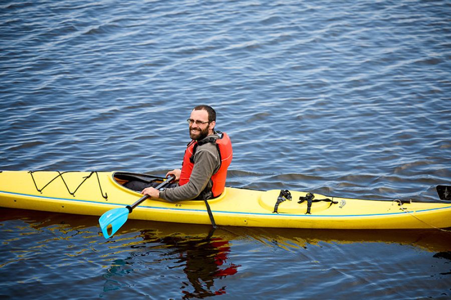 Man with brown hair and red life jacket paddles on coastal kayaking tour in Rockport, MA.