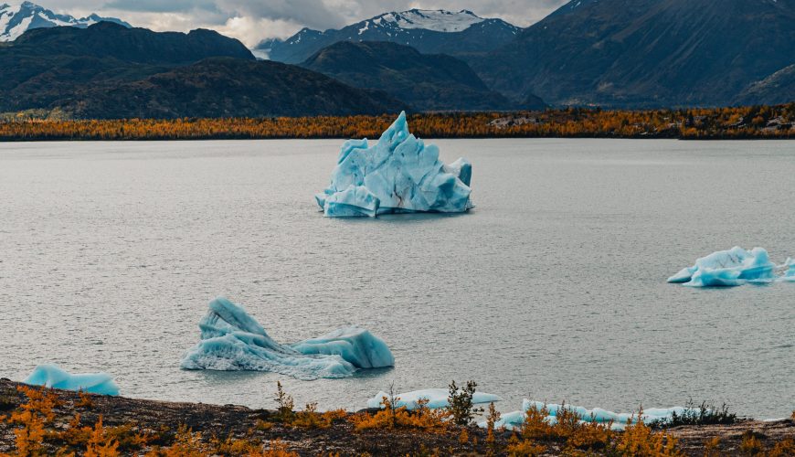 Orange shrubbery on the back of glacial lake with iceberg is best time of year to visit alaska