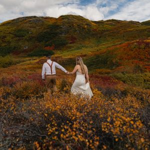 couple walks through fall foliage after elope in alaska