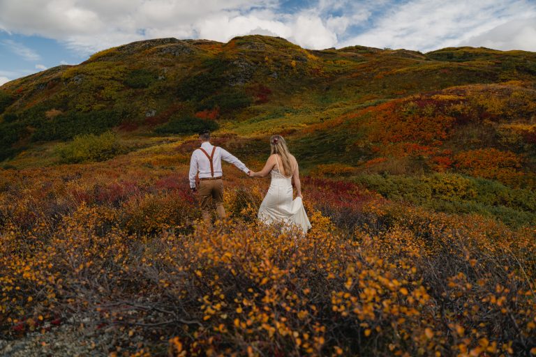 couple walks through fall foliage after elope in alaska