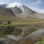 two people cross country biking in field with snow capped mountains in background
