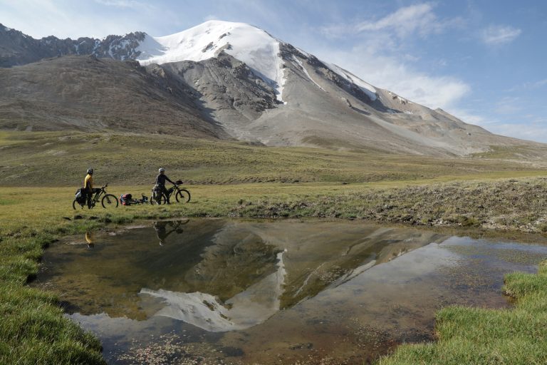 two people cross country biking in field with snow capped mountains in background