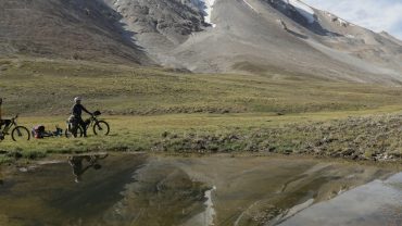 two people cross country biking in field with snow capped mountains in background