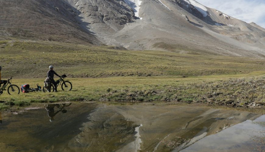 two people cross country biking in field with snow capped mountains in background