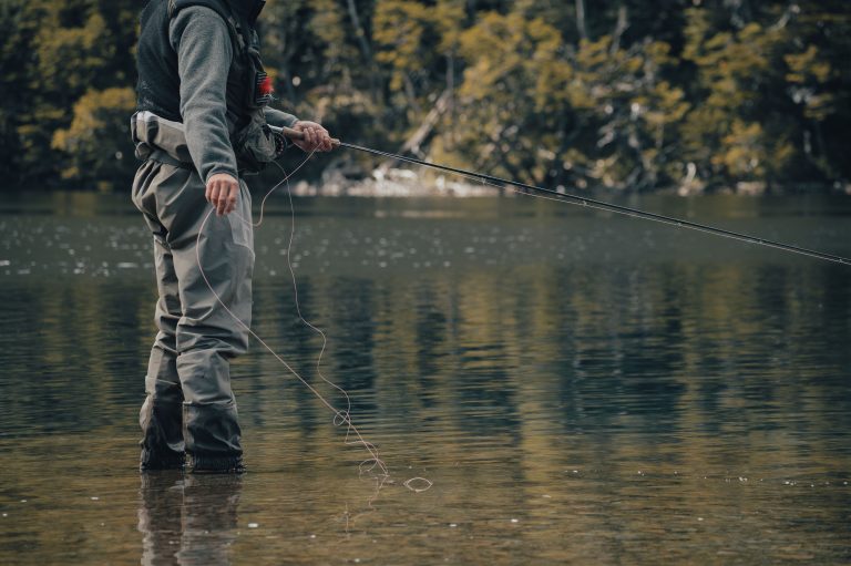 person fly fishing standing in river in waders