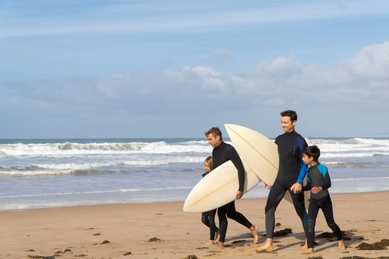 father and two kids in dry suites and surd boards walking on beach to go surfing